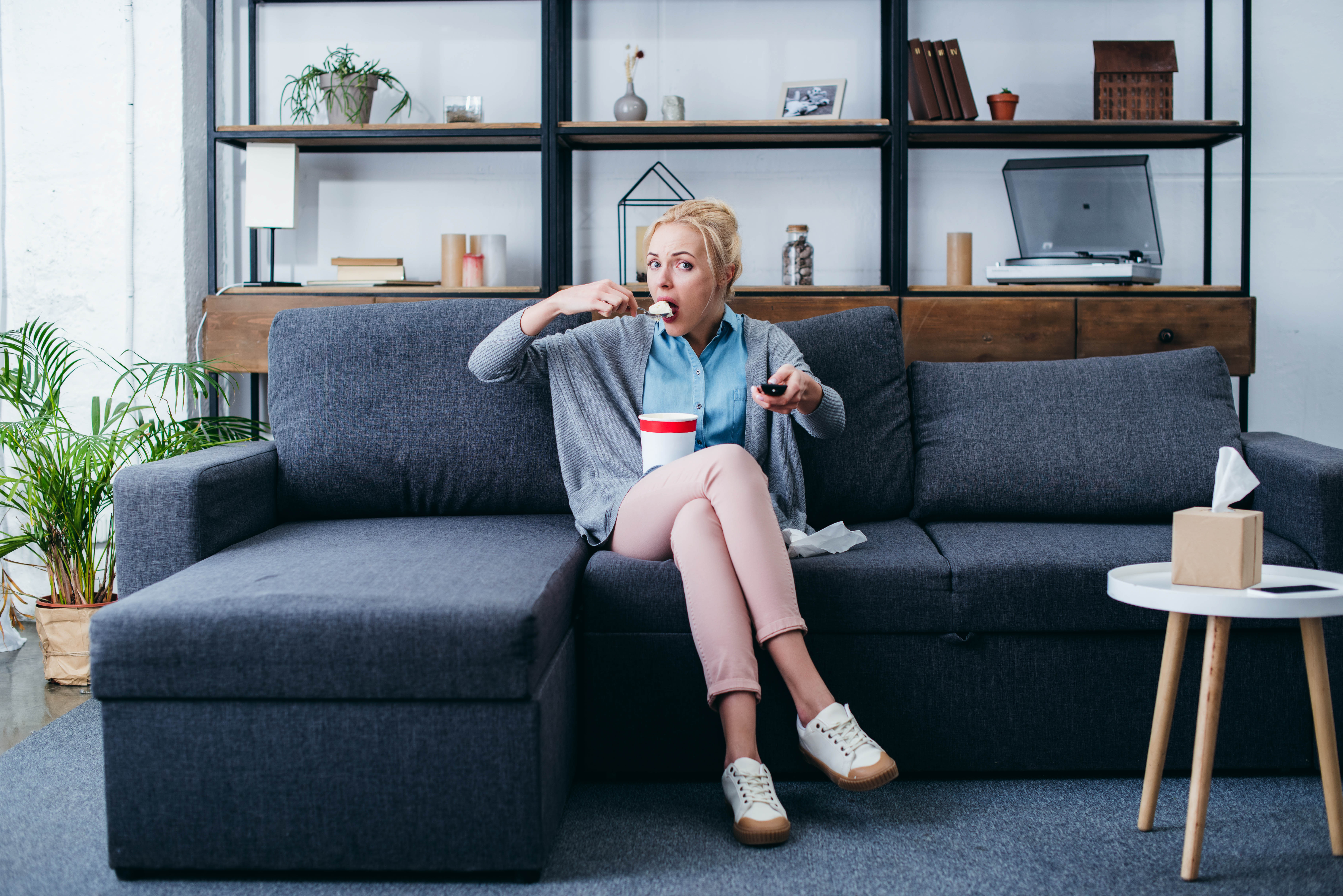 Woman sitting on the couch with a pint of ice cream, scrolling through the tv with the clicker in her hand